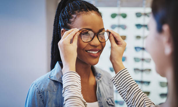 Attractive young African woman selecting glasses Attractive young African woman selecting glasses with the help of an optometrist in a store trying on different frames optometry stock pictures, royalty-free photos & images