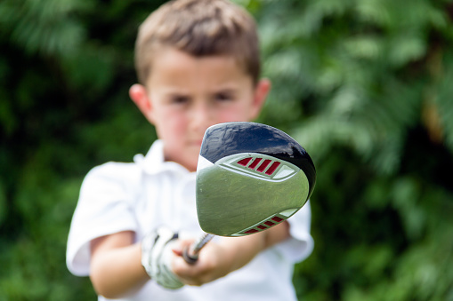 Close-up of golf driver club head held by little boy golfer - selective focus