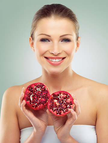 A closeup view of three pomegranates and a glass full of pomegranate seeds