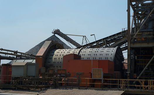 Large SAG/ ball mill crushes rock with a conical crushed ore stockpile in the background during the processing of copper ore at a large open cast African copper mine.