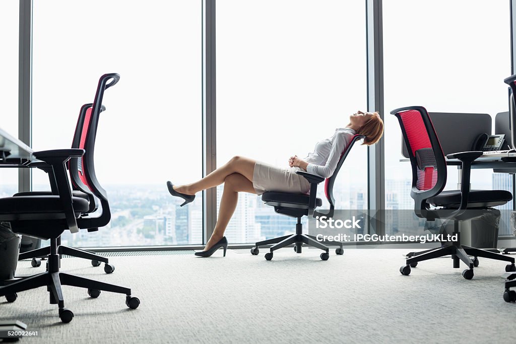 Young businesswoman leaning back in chair at office Full length side view of young businesswoman leaning back in chair at office Office Chair Stock Photo