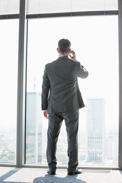istock mature businessman using cell phone white standing near window 520022653