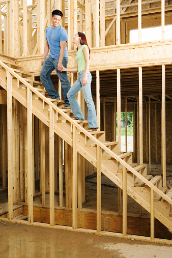 Young couple holding hands on stairs of new home construction