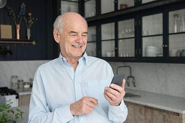 istock Senior man holding smartphone smiling in modern kitchen 520050314