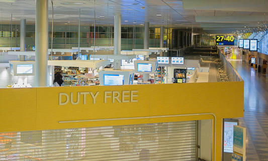 Duty-free store is a retail store located in Munich airports, that offers tax and duty-free goods to international travelers who are leaving or entering the country and typically include products such as alcohol, tobacco, perfume, cosmetics, electronics, and luxury items such as jewelry and watches. A few person shopping inside.