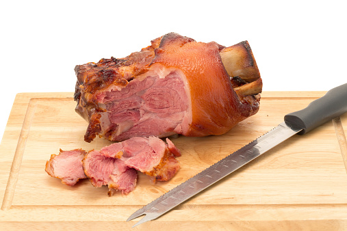 A ready to eat roasted pork gammon joint on a wooden cutting board with a few slices having been cut from it