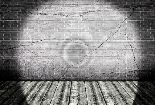 Wooden floor with cracked brick wall illuminated using torch