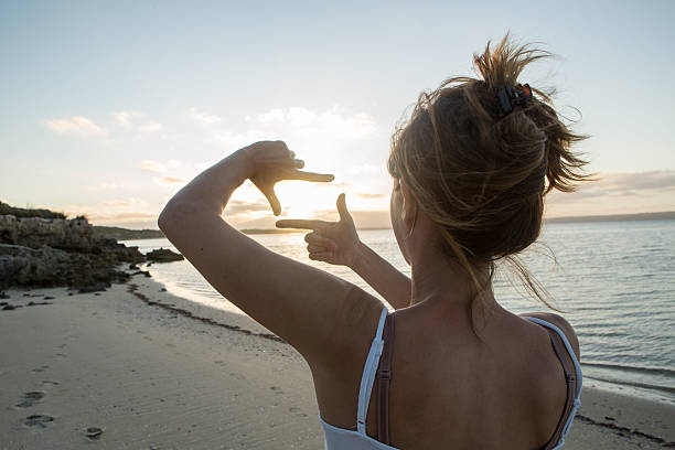 istock Girl on beach makes finger frame towards sun 520096380