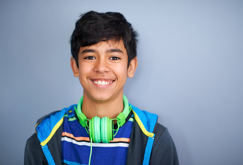 A cute young preteen boy standing and smiling against a grey background