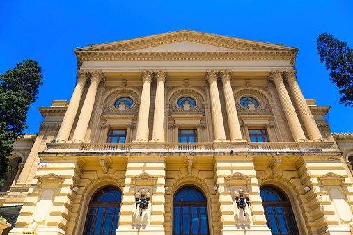 Marble statues of Plato and Socrates, ancient Greek philosophers, seated in chairs, in front of main entrance to Academy of Athens, national highest research center of Greece. Neoclassical architecture. Bright summer daylight, majestic blue sky.