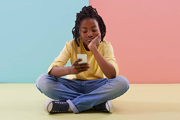 Need more apps... Studio shot of a bored young teen using his smartphone kid sitting cross legged stock pictures, royalty-free photos & images