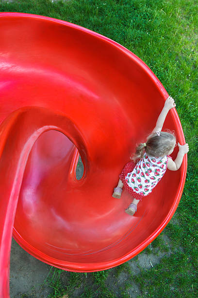 Overhead shot of little blonde girl sliding down playground slide Overhead shot of little blonde girl is sliding down red plastic spiral playground slide school sport high up tall stock pictures, royalty-free photos & images