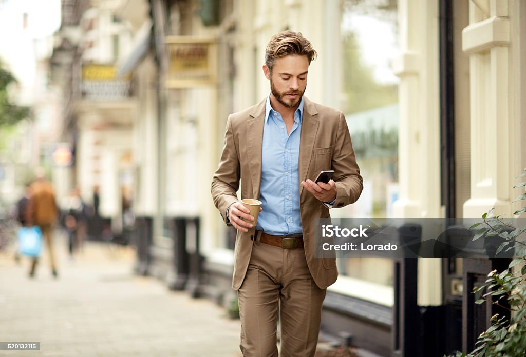 Young man checking the phone in a street Young, well dressed, handsome, bearded man checking his phone outside a local cafe on a european street in the early evening Adult Stock Photo