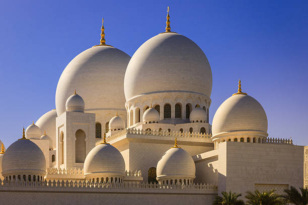 Abu Dhabi, UAE - Zayed Mosque domes, external view Abu Dhabi, UAE - December 29, 2010: The marble domes of Sheikh Zayed mosque in the capital city of Abu Dhabi, in the United Arab Emirates, as viewed from outside the mosque complex. Bright sunlight hits the domes from a side emphasising their Moroccan architectural style. Gold plated crescent moons can be seen atop the domes. Photo shot in the morning sunlight, against a clear blue sky. Horizontal format; no people. grand mosque stock pictures, royalty-free photos & images