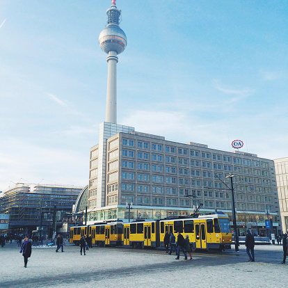 Berlin, Germany - February 1, 2014: Tourist and shoppers walking over Alexanderplatz, Berlin where a yellow tram arrived. Alexanderplatz is a large public square and important transport hub in the central distric of Berlin. Shopping mall and Television tower visible in backgound