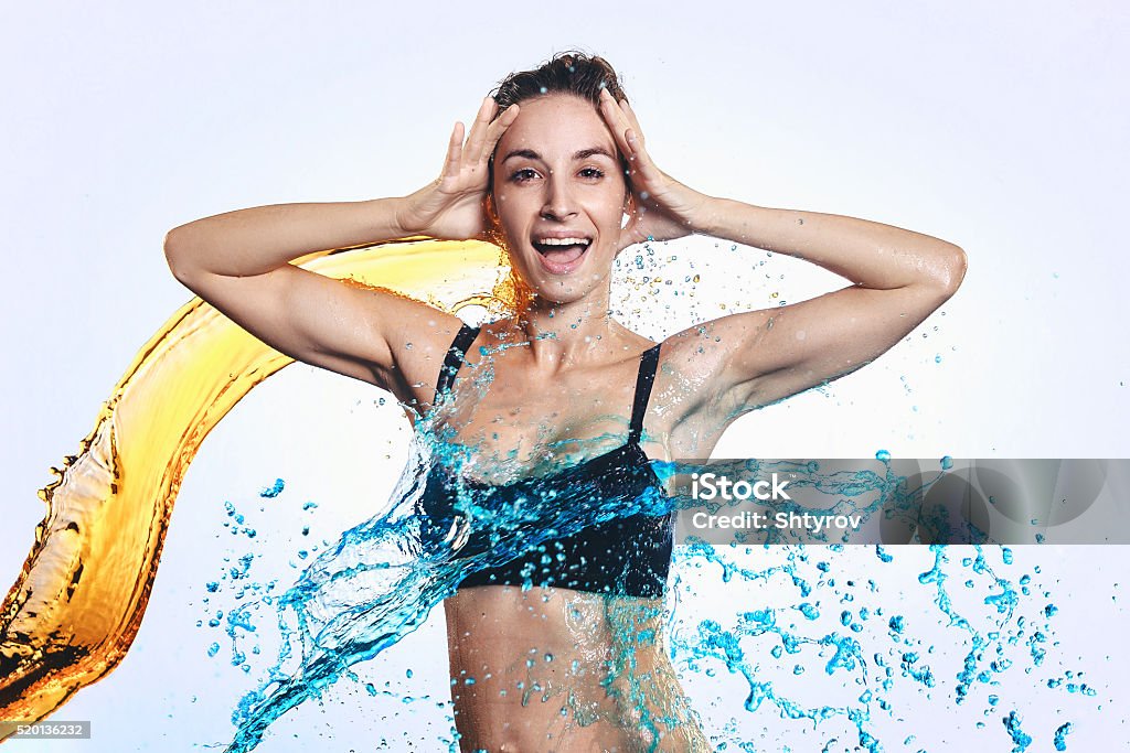 The young woman of a sports constitution in water splashes. The young woman of a sports constitution in splashes in color water. Adult Stock Photo