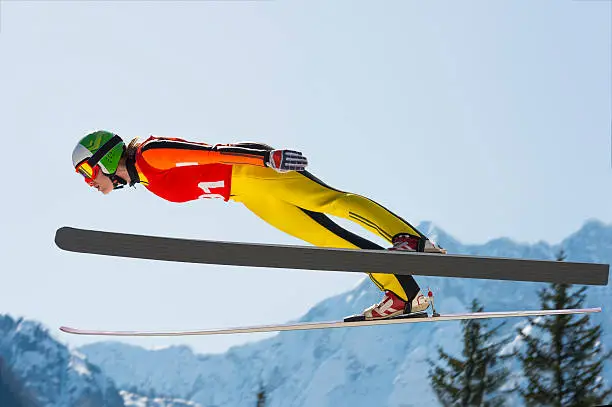 Side view of young female ski jumper during the long ski jump against the sky and mountains