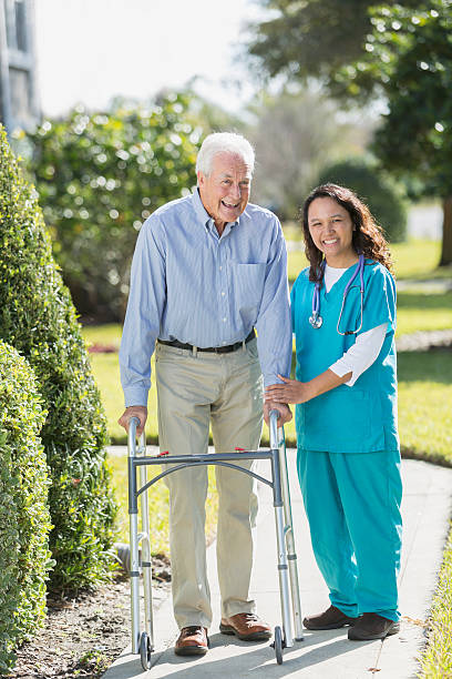 istock Female nurse helping senior man using walker outdoors 520136482