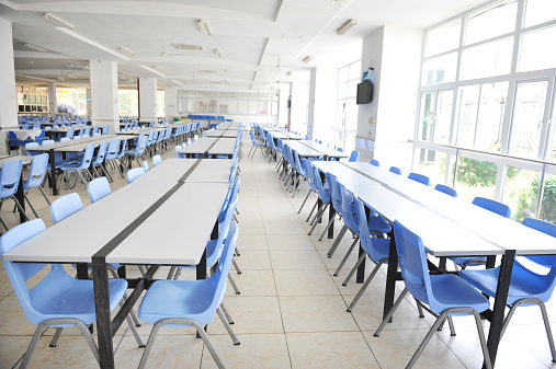 Clean school cafeteria with many empty seats and tables.