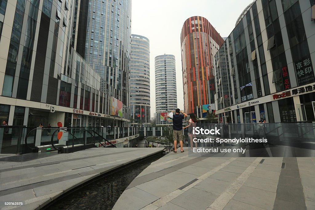 Sanlitun Soho in Beijing Beijing, China - September 11, 2014: Sanlitun SOHO comprises of five shopping malls and nine office/apartment buildings of varying heights. A roller skating rink and outdoor waterscaped courtyard link the malls, forming what will be the liveliest pedestrian shopping street and leisure square in Beijing. Sanlitun SOHO is set to be the area’s colossus, regardless of whether this is defined in terms of the scope of its retail, sheer size, building exterior, or brand influence. People can be seen on the street. Apartment Stock Photo