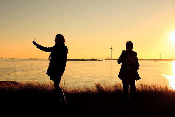 Selfie in the sunset Gothenburg, Sweden - September 3, 2014: Two adult women taking a selphie on the island in the Gota bay. Windmill power generators in the background. västra götaland county stock pictures, royalty-free photos & images
