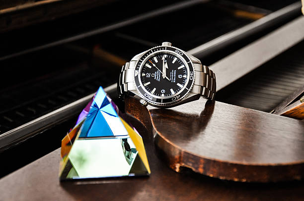 Munich, Germany - January 8, 2011: Omega Seamaster Planet Ocean wristwatch lying on a grand piano with a glass pyramid standing next to it.