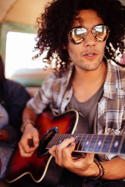 istock Hipster Man Musician Playing Guitar in Van on road trip 520173128