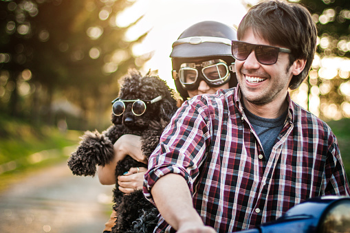 Happy couple with a dog on a scooter at summer vacation