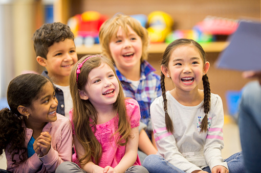 A multi-ethnic group of elementary age children are listening to their teacher read a storybook in class.