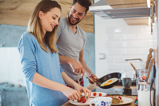 Young happy couple preparing breakfast for their family. Wearing pajamas while standing in the kitchen.