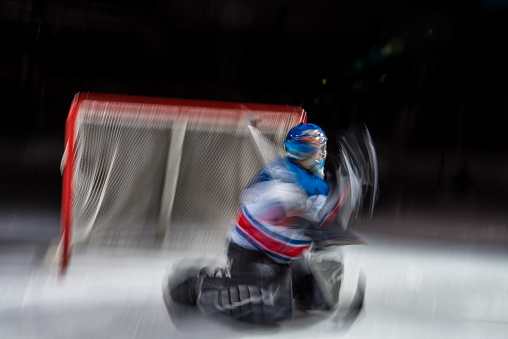 Ice hockey goalkeeper trying to catch puck in ice hockey stadium, blurred motion.