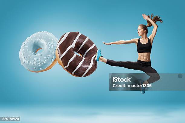 Fit Young Woman Fighting Off Bad Food On A Blue Stock Photo - Download Image Now - Dieting, Healthy Lifestyle, Sugar - Food