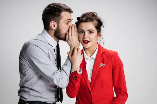 Young man telling gossips to his woman colleague at the office. Intrigues and wasting time concept