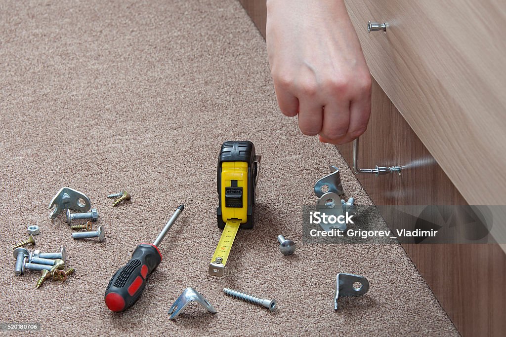 Close-up of carpenter hand tightens fixing screw, using key furniture. Key furniture screws,  close up carpenter hand  tightens screw with an allen wrench,  screwing up of furniture screw. Activity Stock Photo