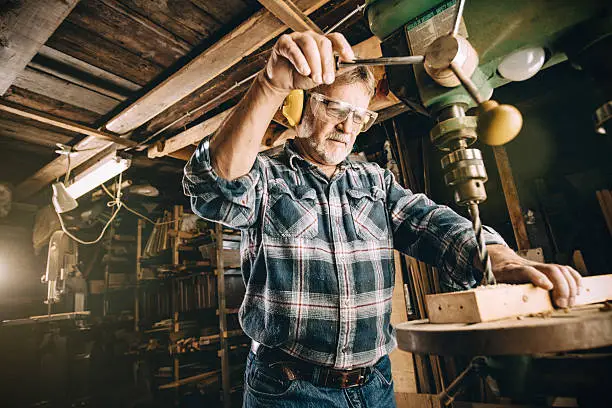 Photo of Mature carpenter using drill press in workshop
