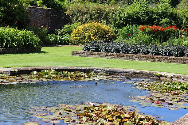 Photo showing an ornamental garden pond with crystal clear water and aeriation provided by an attractive fountain.  Lots of water lily pads provide shade for the goldfish, while the edge of the liner is hidden by paving stones.