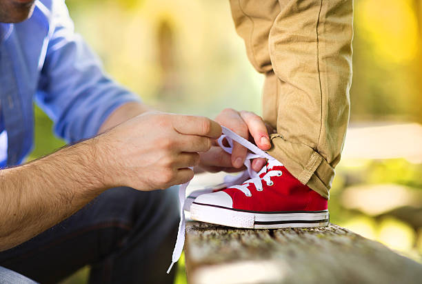 Father and son in nature Father is helping his son to tie his shoes in summer nature child tied up stock pictures, royalty-free photos & images