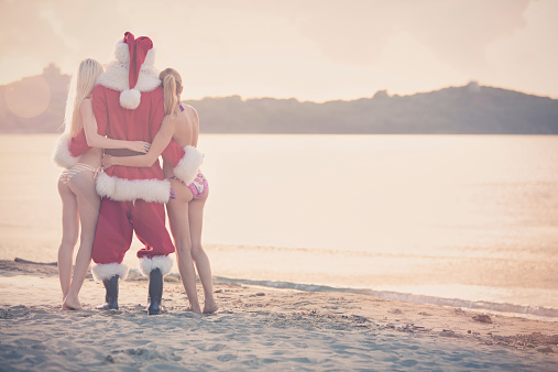 Santa Claus and beautiful girl standing at sunset on shore