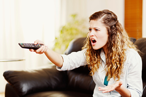 This cute curly-haired woman holding a TV remote control gestures in frustrated irritation at something she has seen  - or not seen - on the screen.