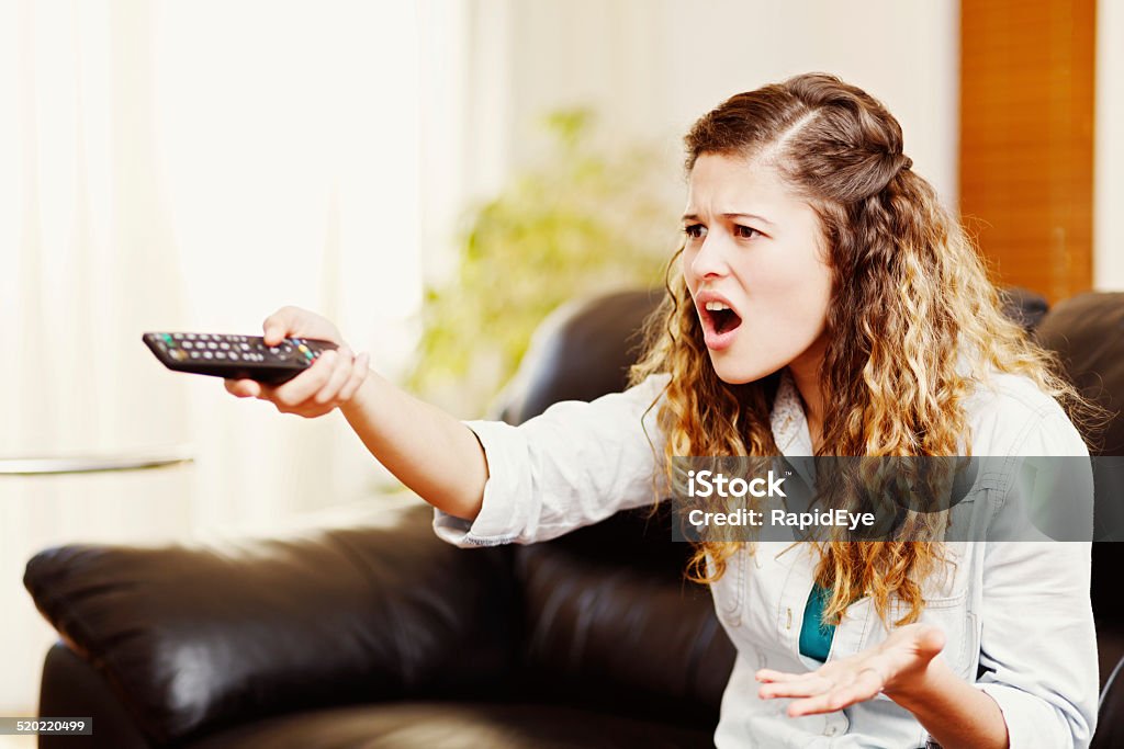 WTF? Where's my show? Irritated young woman points remote control This cute curly-haired woman holding a TV remote control gestures in frustrated irritation at something she has seen  - or not seen - on the screen. Television Set Stock Photo
