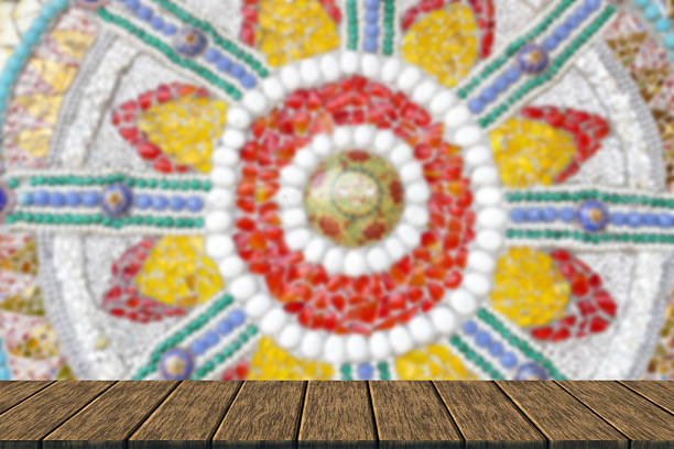the art design of the colorful broken tile, bead, bowl and stone decorating on wall as blur background with wood table top for display or montage your product (art decoration at the wall of the building at Wat Phra That Pha Son Kaew temple)