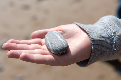 Close up image of  young boys hand holding pebbles from a beach