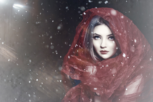portrait of surreal red riding hood with misterious look posing in the forest, photo taken in the forest while snowing.