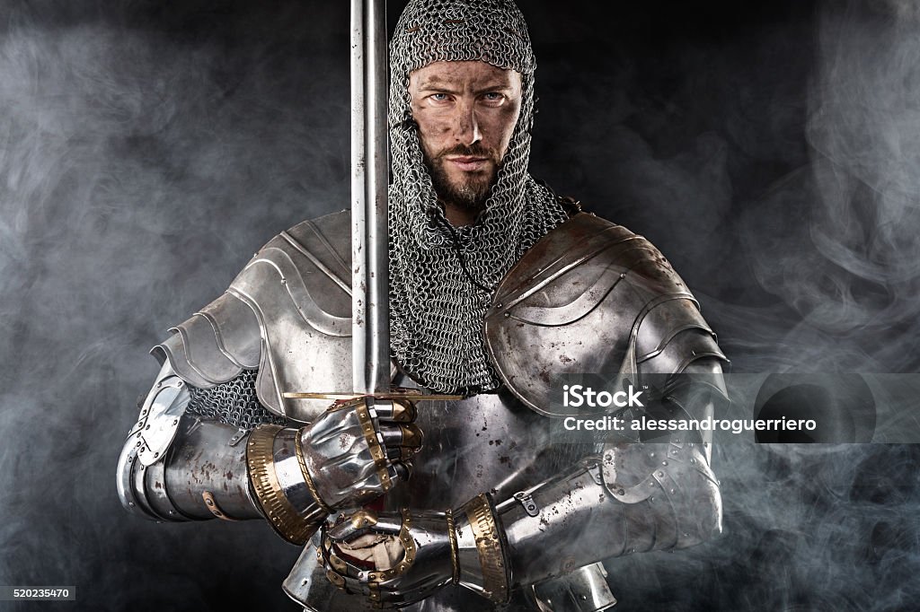 Medieval Warrior with Chain Mail Armour and Sword Portrait of Medieval Dirty Face Warrior with chain mail armour and red cross on sword. Cloud smoke on Dark Background Knight - Person Stock Photo
