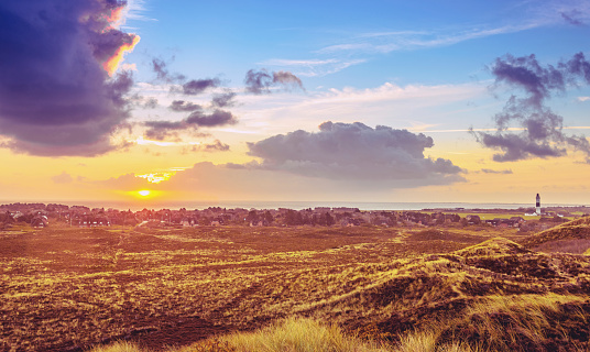 Elevated view over dunes on the sunrise over Kampen on Sylt on a beautiful autumn day. The Wadden sea, the lighthouse and village of Kampen are illuminated by sunlight. 