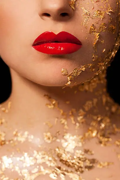 Beautiful woman, creative beauty close up with red lips and gold on face and neck.