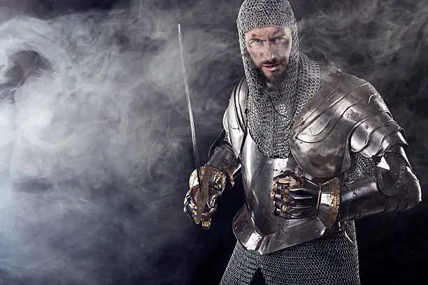 Portrait of Medieval Dirty Face Warrior with chain mail armour and red cross on sword. Cloud smoke on Dark Background