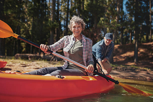 felice donna senior in kayak sul lago - canoeing canoe senior adult couple foto e immagini stock