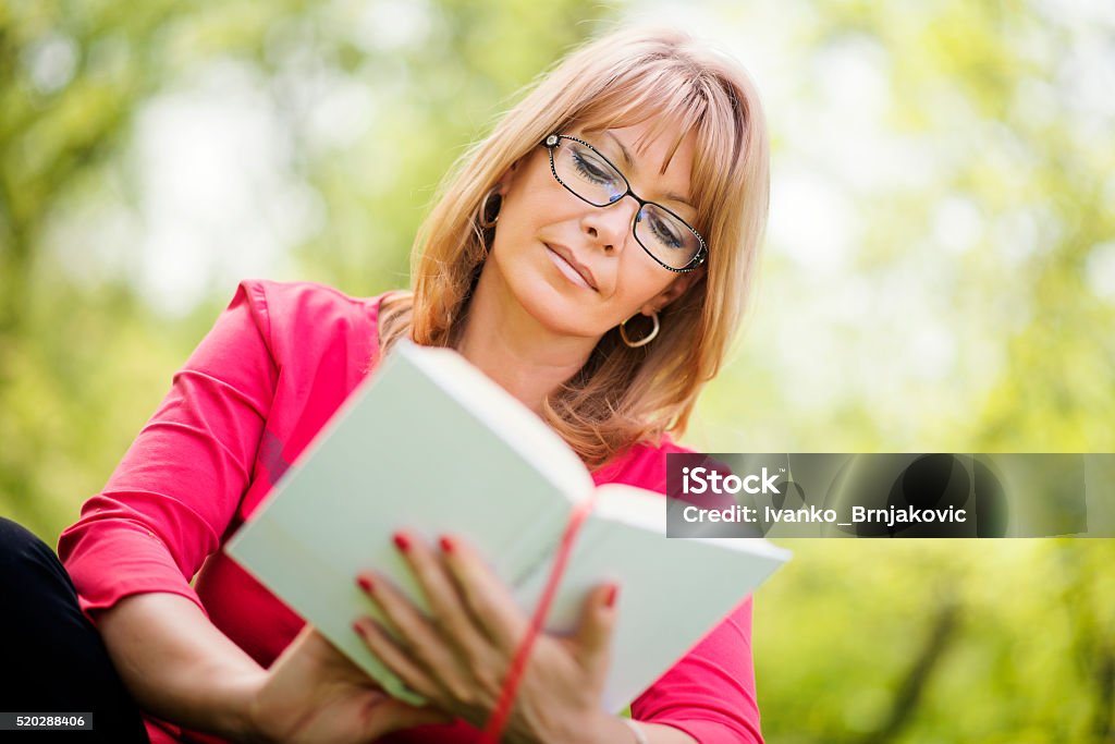 Woman reading a book in the park Beautiful mature woman.Happy woman reading a book during springtime in nature. 40-49 Years Stock Photo