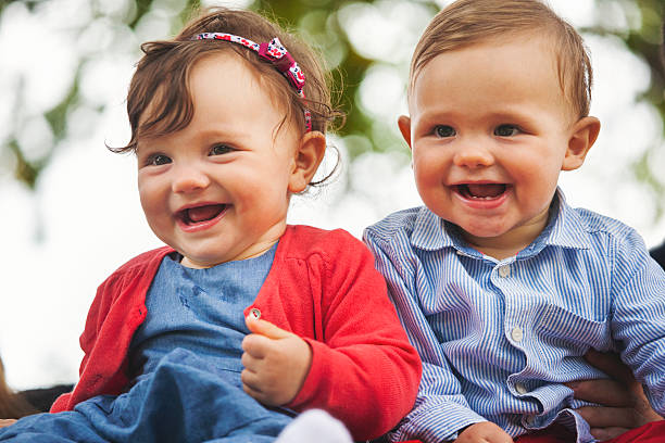 Twin baby smiling for the camera Family portraits outdoor. Very Shallow DOF. Developed from RAW; retouched with special care and attention; Small amount of grain added for best final impression. Adobe RGB color profile. twin photos stock pictures, royalty-free photos & images